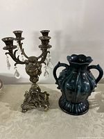 Both items displayed together on a table with a lace tablecloth: ornate brass candelabra with crystal jewels and blue-green handled vase.