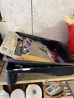 Paint trays stacked with scrapers and stir sticks on wooden shelf against wall