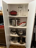 Open cabinet view showing the assortment of cookware including pots, strainers, metal and plastic bowls, and glass vases.