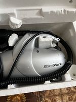 Silver Shark Steam Cleaner main unit inside white styrofoam packaging with black coiled hose.