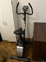 Front view of stationary exercise bike against white wall between cabinet and dresser