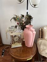 Photo showing the tabletop clock, pink vase, and peacock feather vase arranged on a wooden round table in a living room.