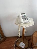 Wide view of the hexagonal telephone table with the white large-button landline phone on top, showing the pedestal base and coiled phone cord.
