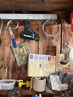 Tools hanging on wooden wall including clamp, caulking gun, screws in packaging, pipe wrench, and decorative pictures.
