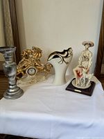 Four items in the lot: silver candlestick, gold-tone horse clock, cream ceramic vase with gold trim, Valentino lady figurine with lamb on wooden base