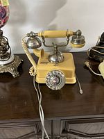 Front side view of yellow vintage rotary telephone with handset on cradle, showing coiled cord and rotary dial with graphic center label.