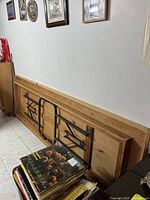 Folded wooden table with visible metal legs and natural wooden finish leaning against a white wall next to some books on the floor.