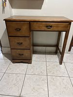 Full front view of wooden desk with four drawers on left side and one wide drawer on right above knee space.