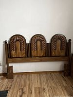 Full frontal view of the wooden headboard showing three arched carved panels and side supports with finials.