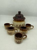 Front view of the 1970s two tone stoneware set showing covered jar, cream pitcher and four small mugs, wheat motif visible