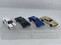 Four Hot Wheels cars: white police car, black police car, blue police car, beige sheriff car, all used and about 3 inches long.