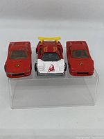 Front view of three Hot Wheels cars: two red Ferraris and one red and white Lamborghini with yellow spoiler, all showing used condition with paint chipping.
