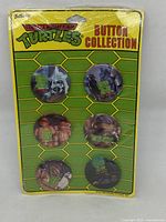 Full package of six TMNT collectible buttons from 1990, sealed in plastic wrap on original cardboard backing.