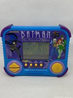 Front view of handheld game showing screen, directional pad, buttons, and Batman artwork