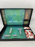 Open Battleship game board with ships placed and red and white pegs in compartments.