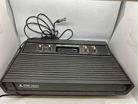 Front and top view of the Atari 2600 console showing control panel, cartridge slot, and attached RF cable with coax connector.