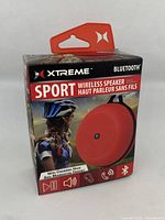 Front view of Xtreme Sport wireless Bluetooth speaker box featuring red speaker with carabiner hook and sport use imagery.