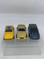 Front view of the three Hot Wheels Camaro cars showing yellow, gold, and blue cars side by side on clear display stand.