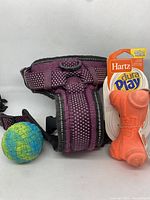 Purple large dog harness with visible wear alongside orange Hartz dura play dog bone toy and multicolor woven ball dog toy