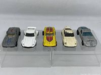 Front view of five diecast cars placed side-by-side on clear stands showing colors and condition