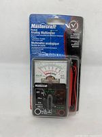 Front view of new Mastercraft pocket analog multimeter in blister pack showing analog needle gauge, settings dial, and attached test leads.