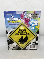 Front view of Nintendo Blue Shell On Board hanging car sign in original packaging with colorful background and warnings on the card backing.