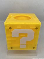 Yellow translucent cube resembling the Super Mario Bros. question mark coin block, showing a white question mark on the front side and round opening on top with maze inside.
