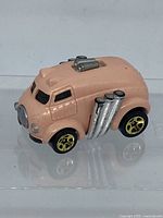 Side view of pink diecast Hot Wheels car showing chrome exhaust pipes and black windows.