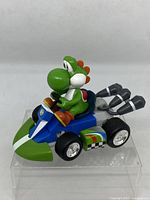 Side angled view of Yoshi sitting in blue and green mini Mario Kart vehicle showing left side and exhaust pipes.