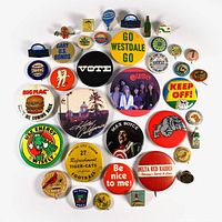 Top view of 38 vintage pinback and butterfly clutch buttons spread out on white background showing various designs, logos, and slogans.