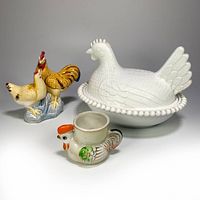 Lot showing all three items: white milk glass hen on nest covered candy dish, ceramic rooster egg cup, and colorful rooster and hen figurine.