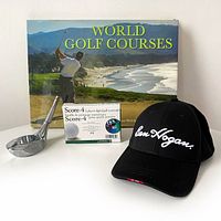 Front view of World Golf Courses book with dust jacket, Shield Fifth Avenue chrome driver ashtray, new Perfect Solutions digital golf scorecard in original packaging, and black Ben Hogan adjustable Velcro baseball cap displayed on white surface.