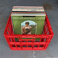 Red plastic crate filled with approximately 40 assorted vintage country vinyl records, showing Mother Maybelle Carter album cover at front.