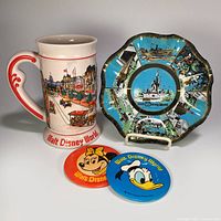 All four items together: ceramic Main Street mug, ruffled glass 7 Kingdoms dish, red Minnie Mouse button, blue Donald Duck button.