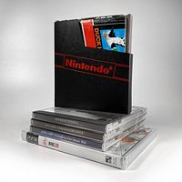 Photo showing the stack of 5 video game cases including Nintendo NES cartridge in sleeve and instruction booklet on top, with four jewel cases below