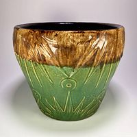 Front view of the planter pot showing brown over green glaze with embossed sun and moon motif.