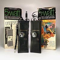 Pair of black Realistic 5-watt 6-channel CB walkie talkies standing upright with their original retail boxes behind them showing front packaging graphics.