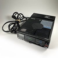 Philips CD10 portable CD player with attached AC10 power adapter showing front controls and connected power cable, viewed slightly from side.