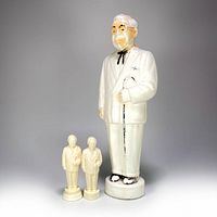 Photo of the full lot with the large Colonel Sanders blow mold coin bank standing behind two smaller Colonel Sanders salt and pepper shakers.