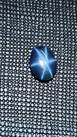 Close-up image of a natural blue star sapphire showing a clear six-ray star effect on the dark textured background.