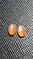 Pair of peach moonstone oval cabochon gemstones placed on textured black surface showing cat's eye light reflection effect.