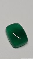 Close-up photo of the natural cushion cut green onyx gemstone showing its deep, vivid green color and polished surface under ambient light.