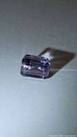 Rectangular emerald cut natural purple amethyst gemstone with good clarity and vibrant color photographed on white background showing facet details.