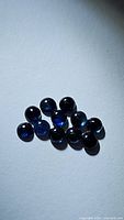 Twelve round natural blue sapphire cabochons arranged closely on a white background under focused lighting, showing deep blue color and polished smooth surfaces.