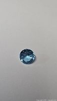 Single natural blue topaz gemstone on white background showing various lighting conditions to highlight color and cut.