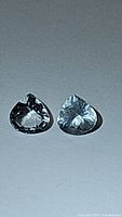 Two pear teardrop cut aquamarine gemstones lying side by side on a plain surface under white light, showing facets and clarity.