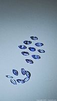 Fourteen marquis cut purple tanzanite gemstones arranged on a white surface taken under natural light