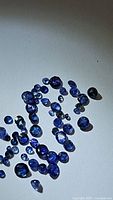 Multiple loose natural cornflower blue Ceylon sapphires in varying sizes and shapes on a white background.