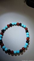 Photo of the natural gemstone bracelet laid flat, showing uniform round beads in shades of red-orange, black, and blue.