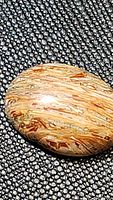 Close-up of oval Indonesian golden opal cabochon on textured black surface showing natural internal striations and polished finish.